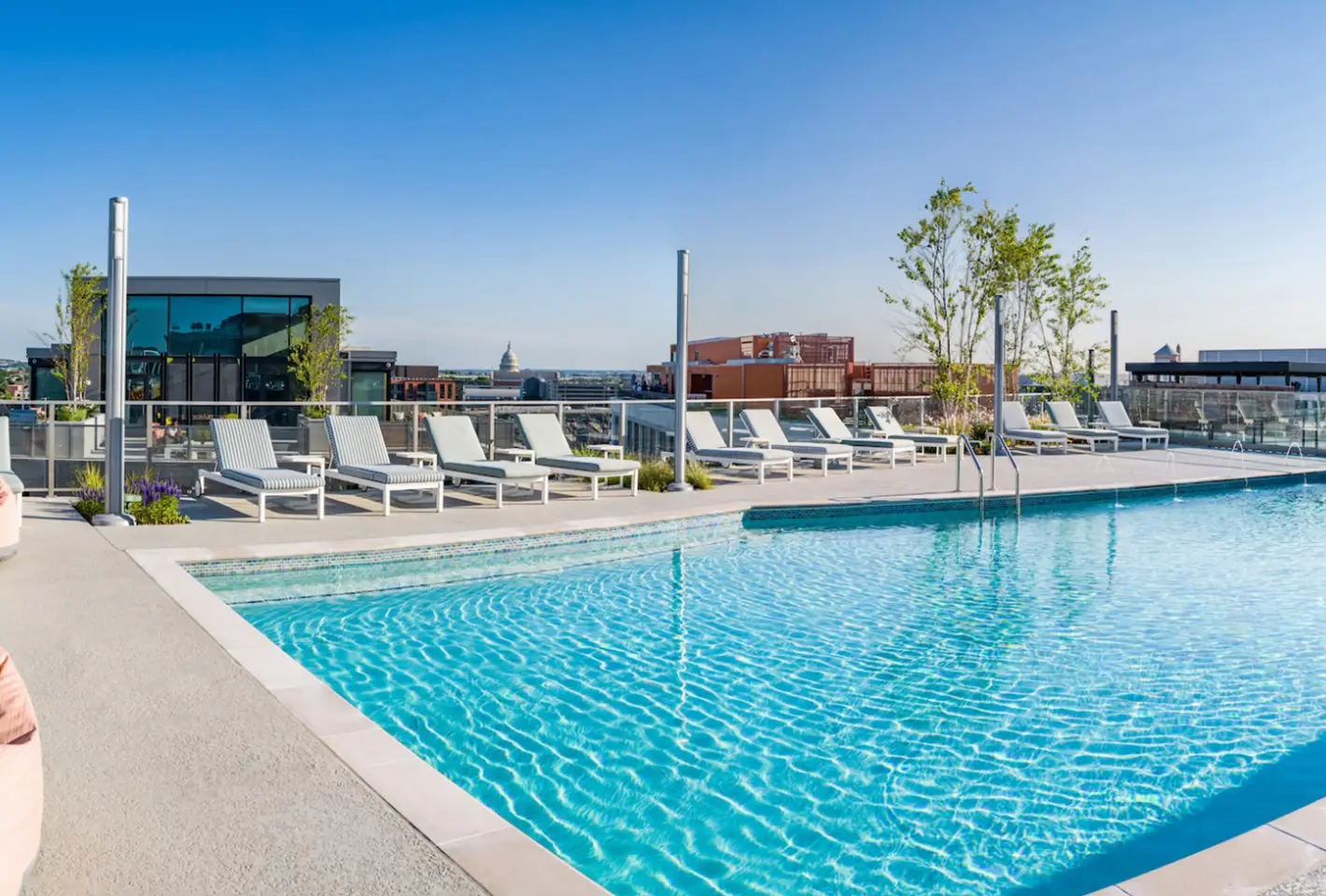 Elegant rooftop pool area featuring sleek lounge chairs with panoramic city skyline in the background