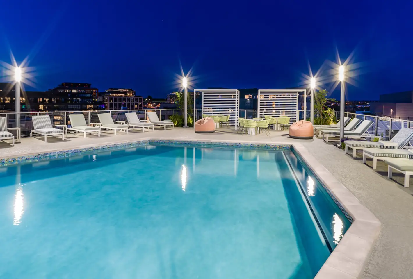Nighttime rooftop pool illuminated by warm lights, showcasing cozy seating and a serene ambiance