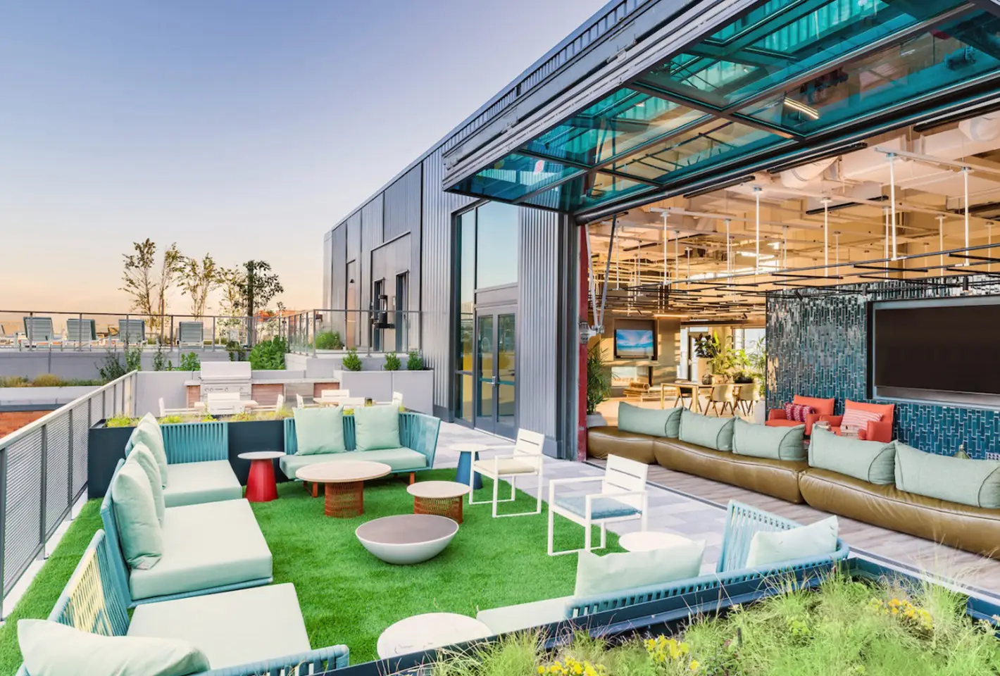 Brightly lit rooftop lounge with open seating, greenery, and contemporary architecture for relaxation