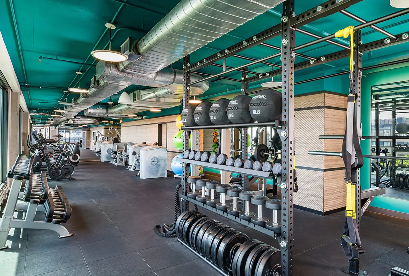 Spacious fitness center with weights, TRX straps, and vibrant teal ceiling for residents