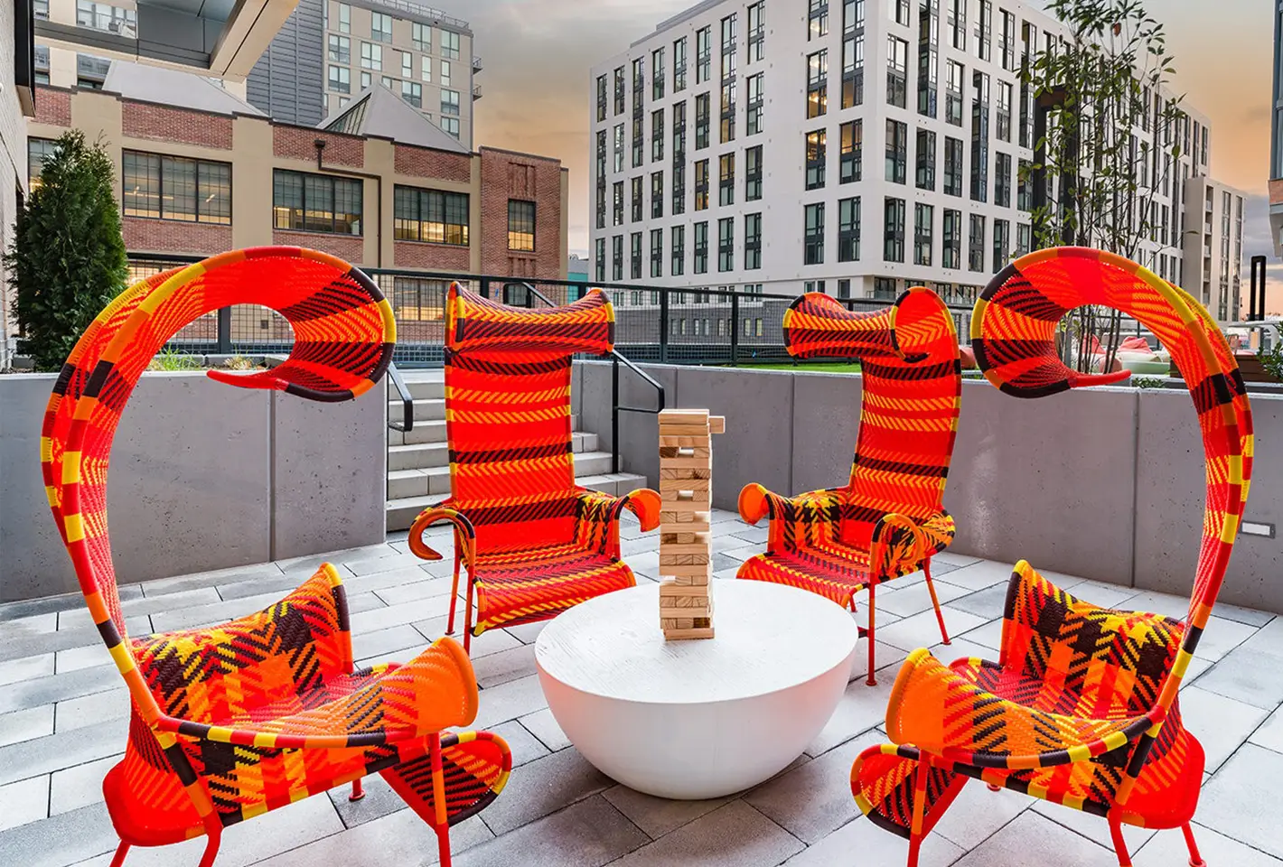 Outdoor rooftop seating with bold red chairs surrounding a round fire pit under evening skies