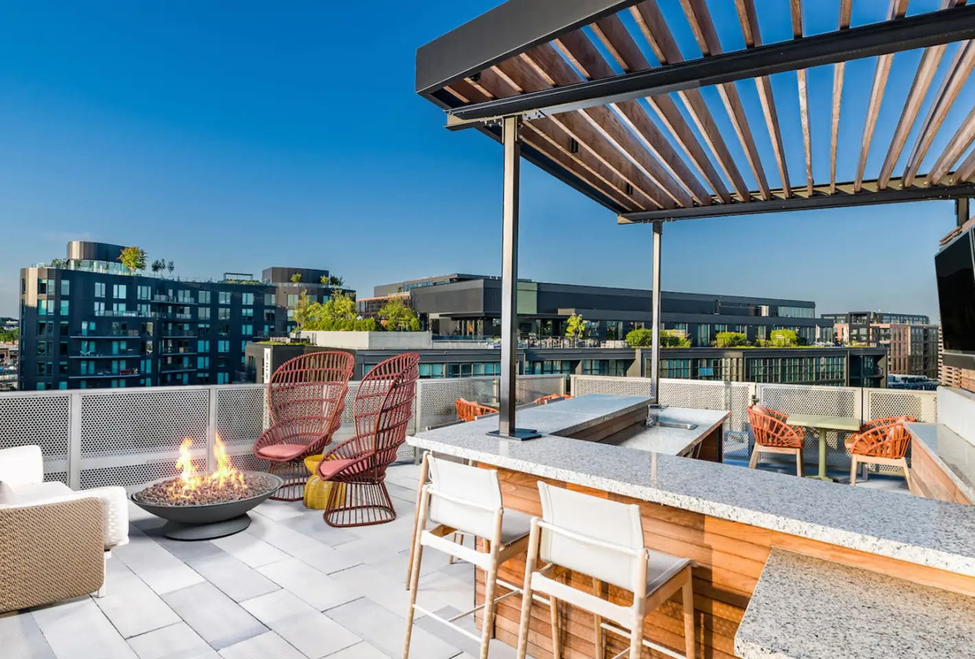 Stylish rooftop lounge with wood pergola, bar seating, and city skyline views under clear skies