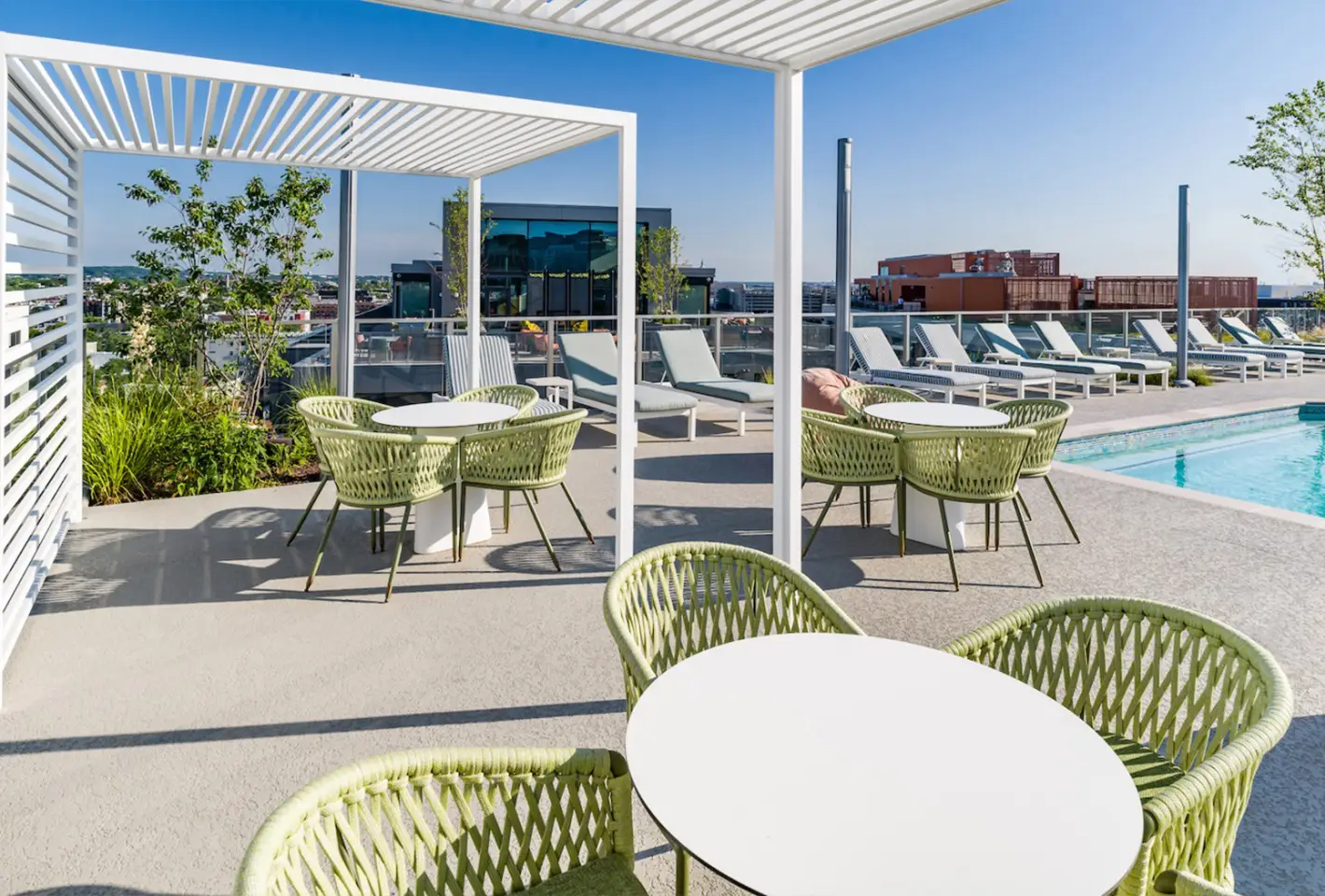 Rooftop poolside retreat with lounge chairs, seating area with round tables, and city views