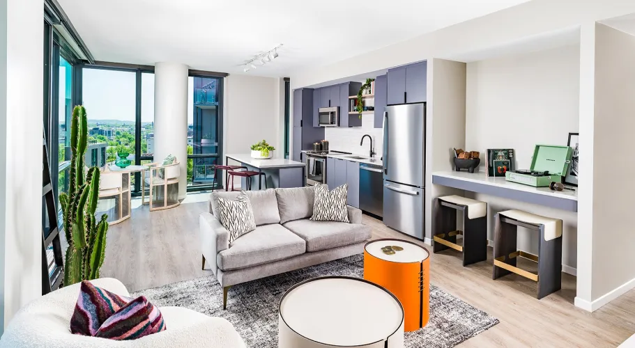Sophisticated living room with bright windows, colorful accents, and a well-equipped kitchen area