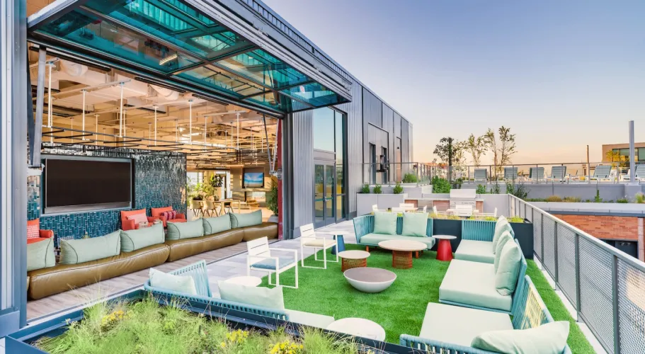 Rooftop lounge with vibrant green turf, modern seating, and sunset views of the city