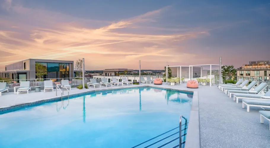 Rooftop pool with modern lounge chairs and a colorful sunset reflecting on the water