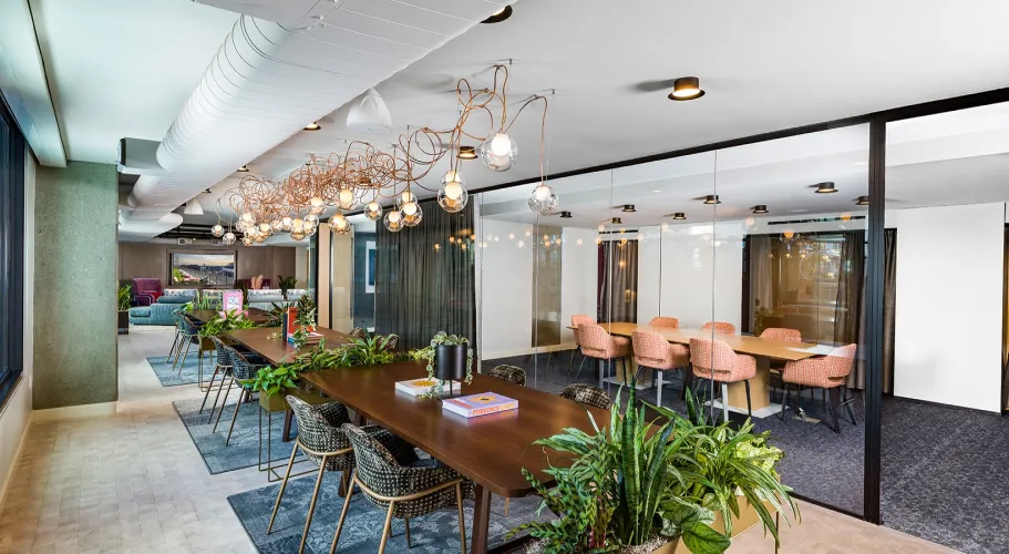 Modern workspace featuring greenery, sleek furnishings, and vibrant overhead lighting for collaboration