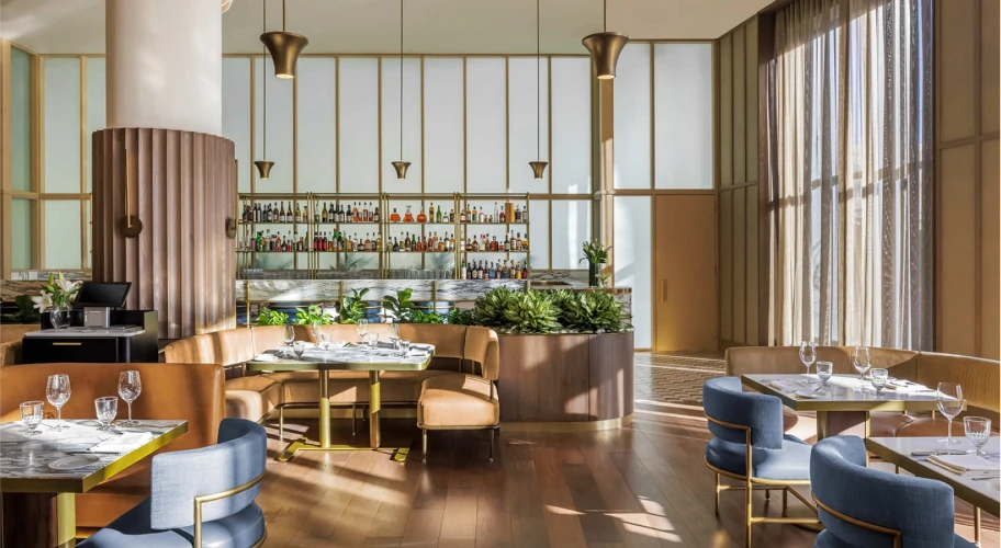 Bright restaurant space with natural light, stylish seating, and a fully stocked bar backdrop
