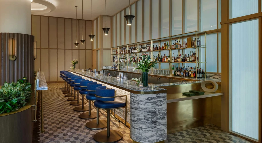 Bright hotel bar with blue stools, marble counter, and a fully stocked liquor display