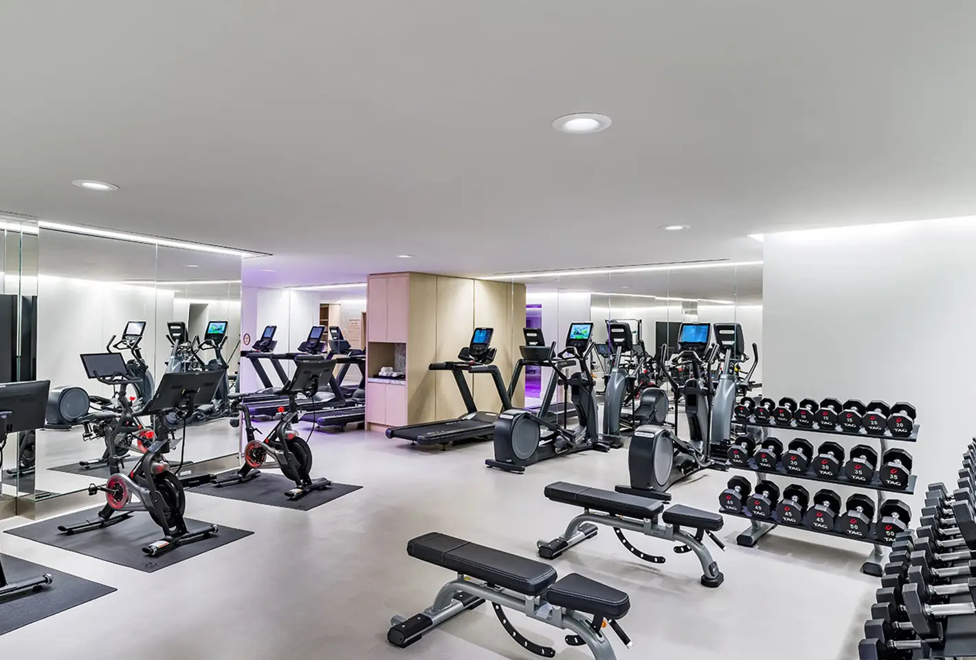 Modern fitness center interior featuring exercise equipment, mirrors, and natural light-filled windows