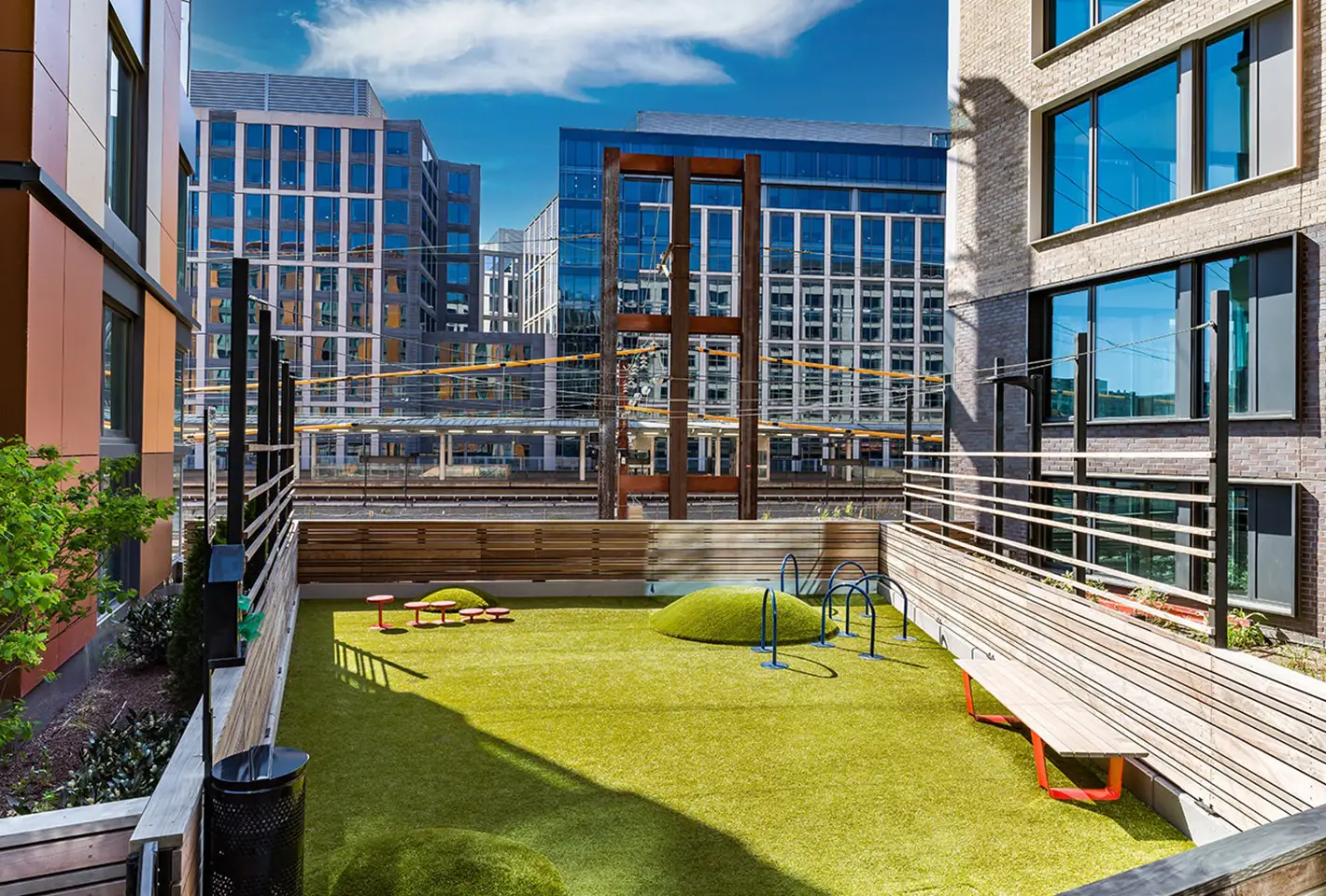 Outdoor pet play area with green turf, playful structures, and surrounded by modern apartment views