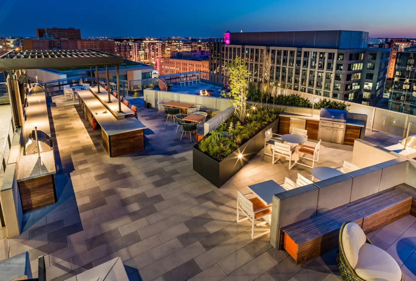 Luxurious rooftop terrace showcasing open-air dining, urban greenery, and evening city lights