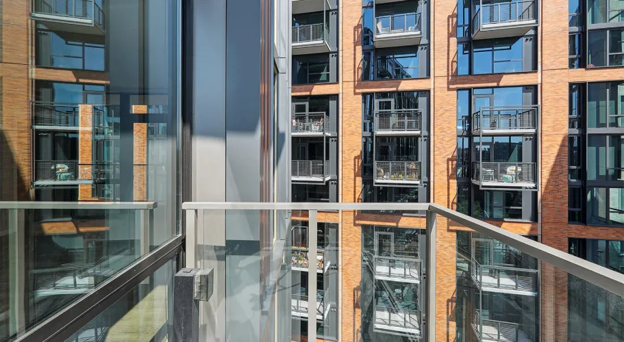 Modern apartment balcony with glass railing and views of adjacent building's architectural design