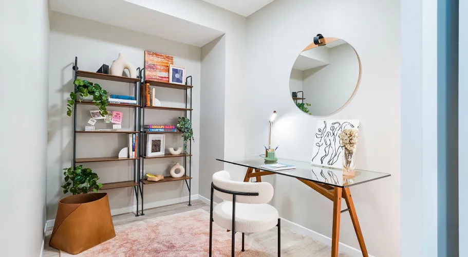 Home office with a modern glass desk, a round mirror and decorative shelving