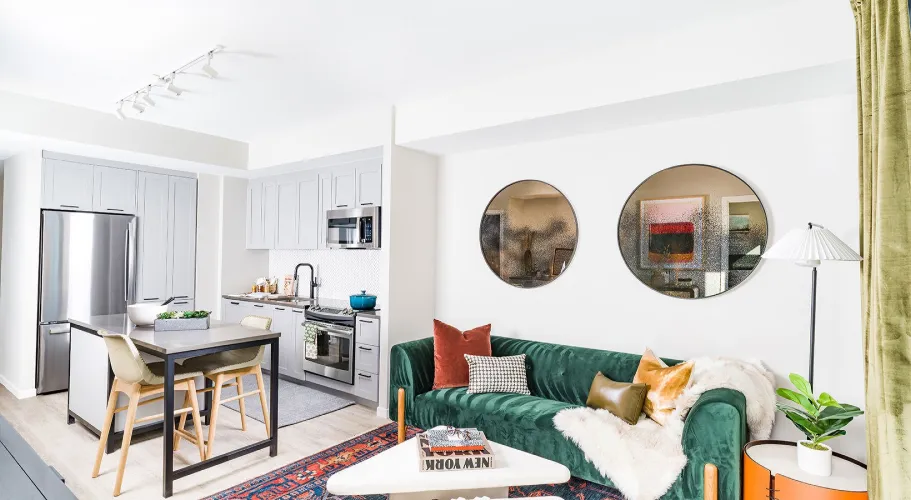 Trendy living room with bold green sofa, modern kitchen, and artistic round mirrors on the wall.