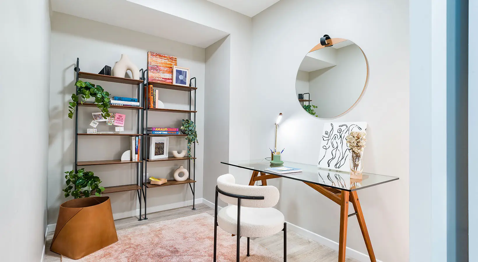 Minimalist home office with glass desk, bookshelves, and a round mirror for decor