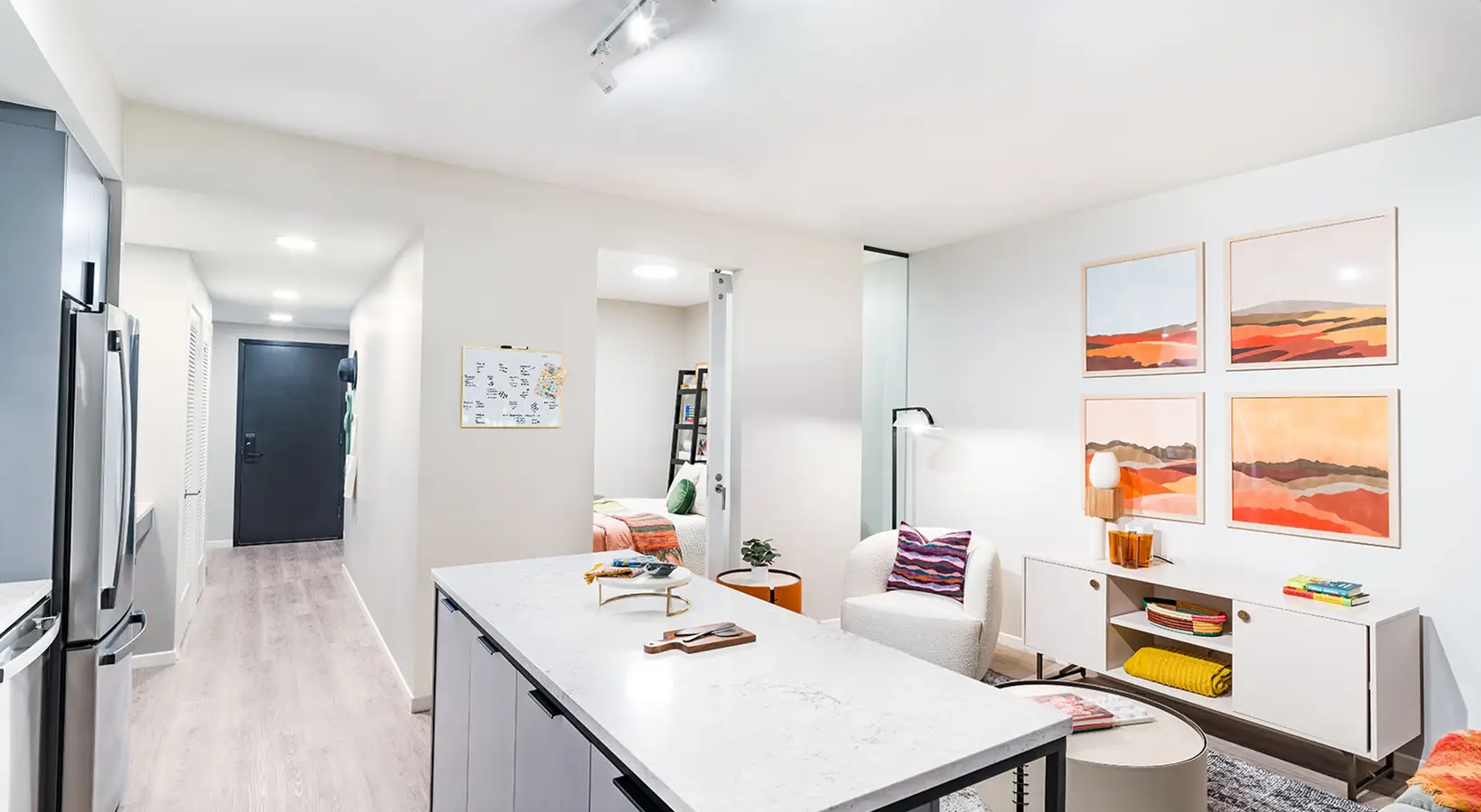 Open living area with white walls, colorful artwork, and light wood flooring.