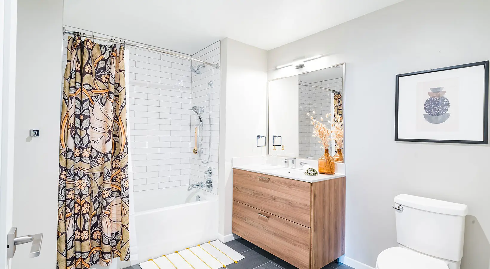 Elegant bathroom with wood-toned vanity, white subway tiles, and floral shower curtain