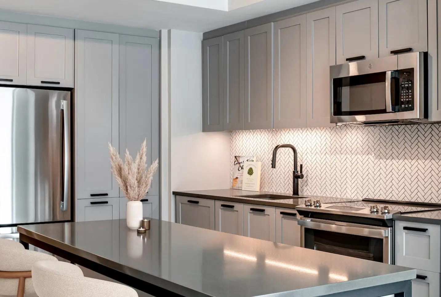 Luxurious kitchen with light gray cabinets, stainless steel appliances, and herringbone backsplash tiles