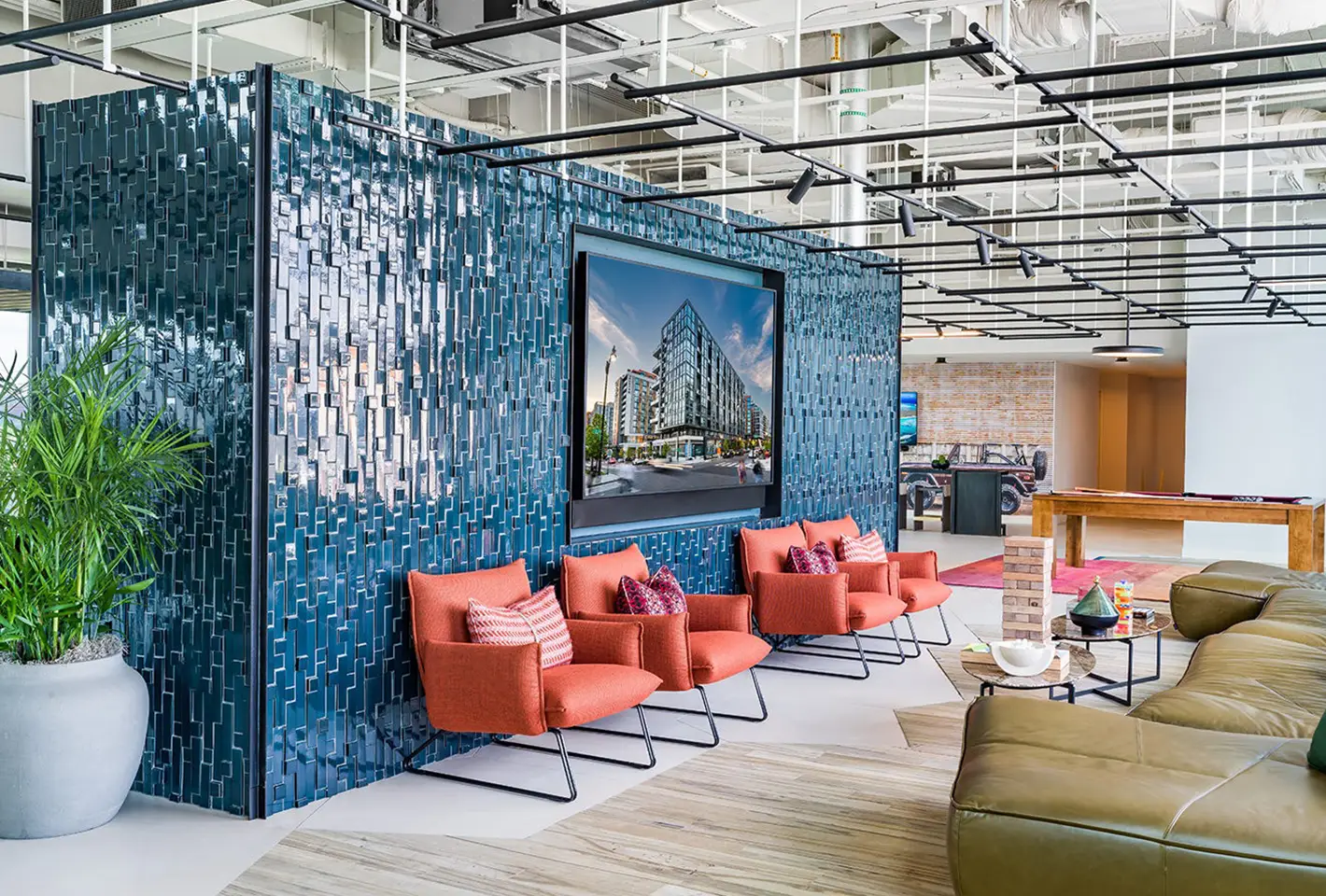 Modern lounge area with orange chairs, textured blue tile wall, and large central screen
