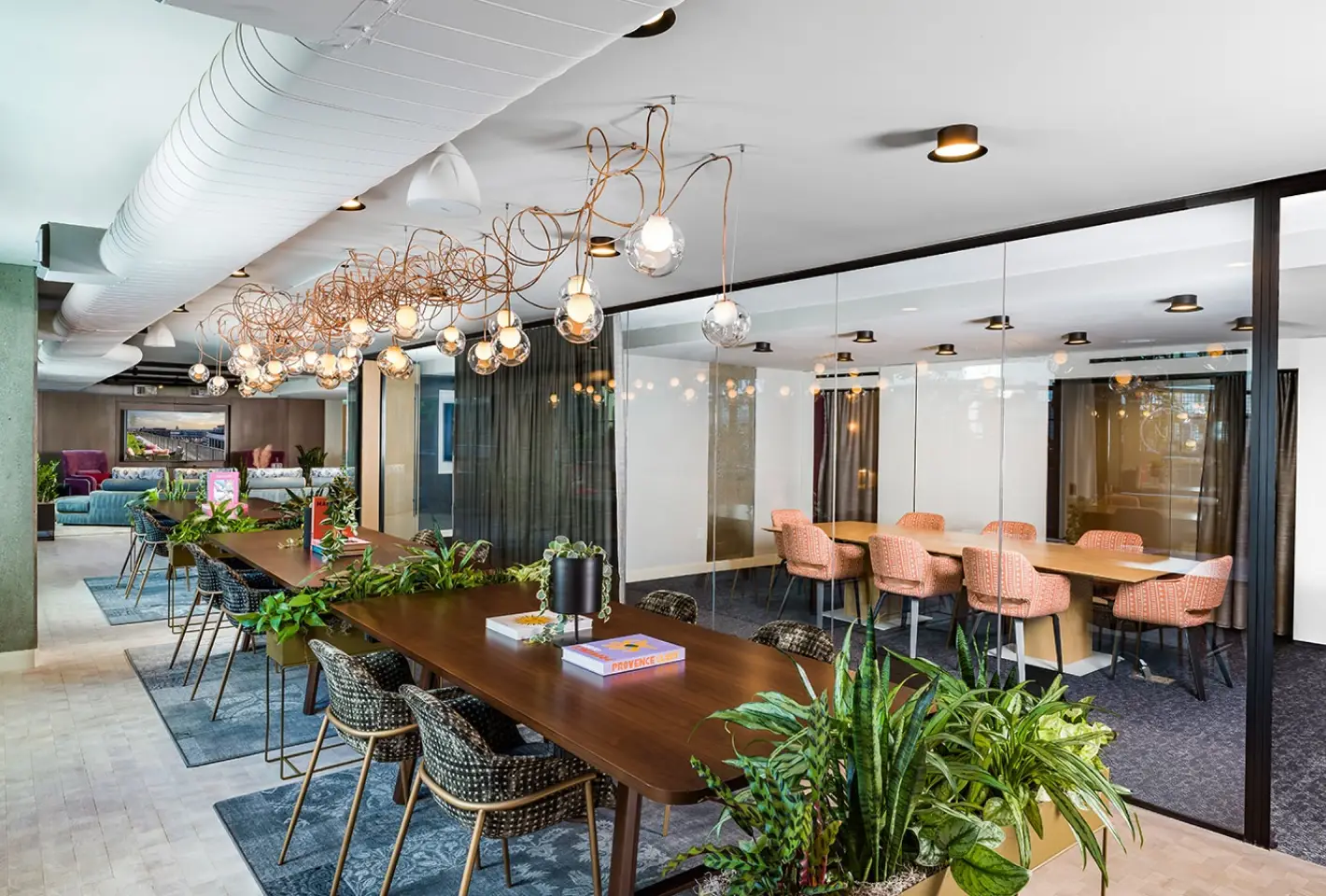 Bright coworking space with open tables, hanging lights, and greenery for a stylish work environment