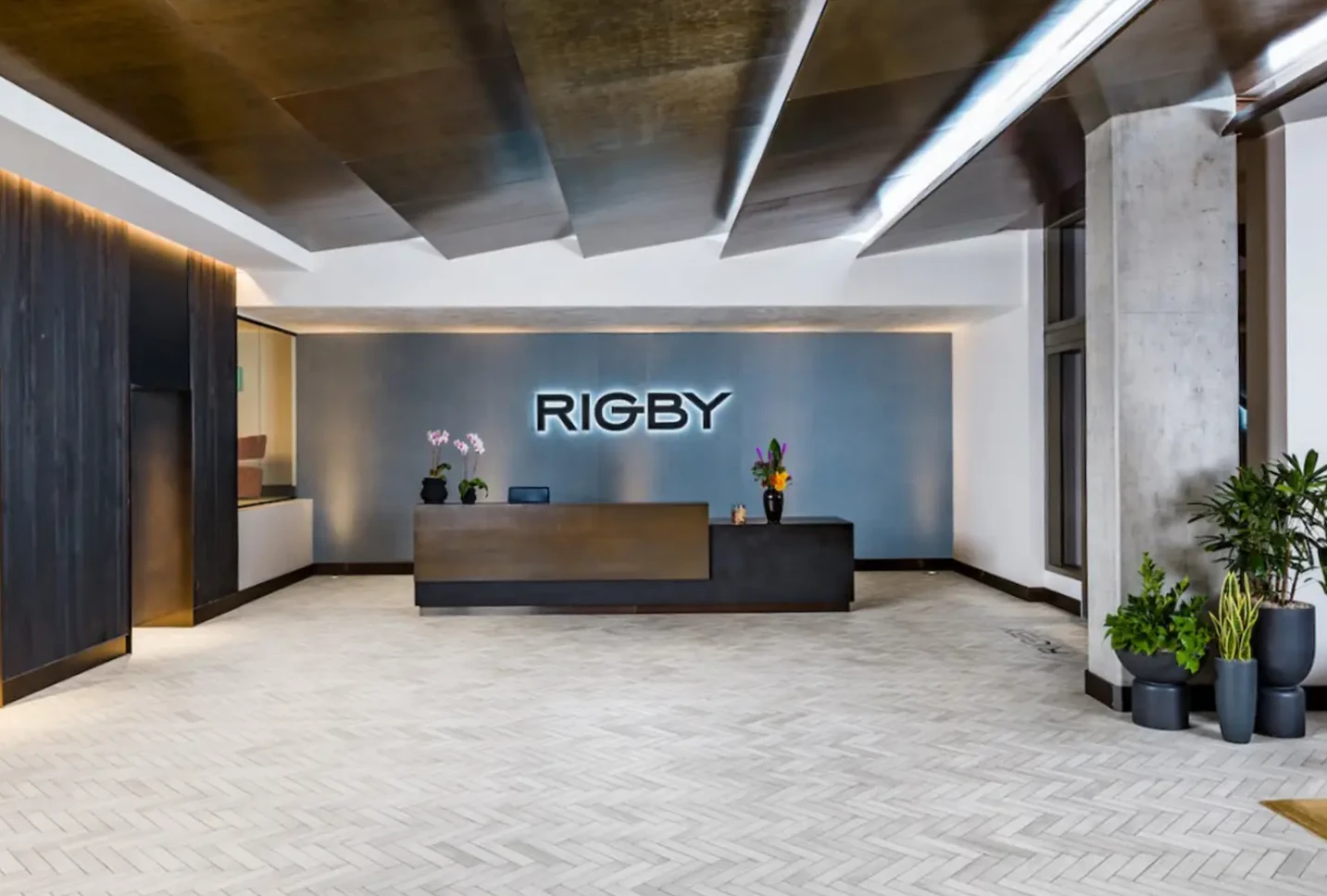 Modern lobby with herringbone flooring and illuminated Rigby sign at the reception desk