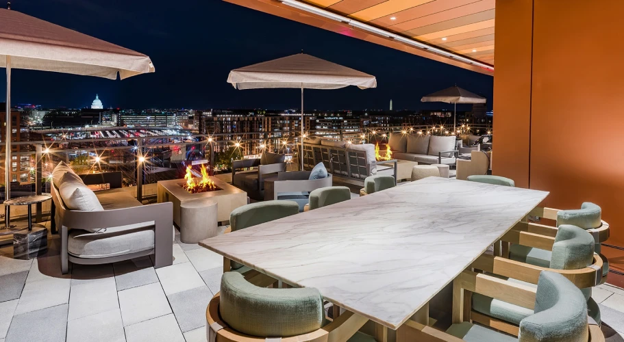 Rooftop terrace at night with ambient fire pits, cozy seating, and illuminated city skyline