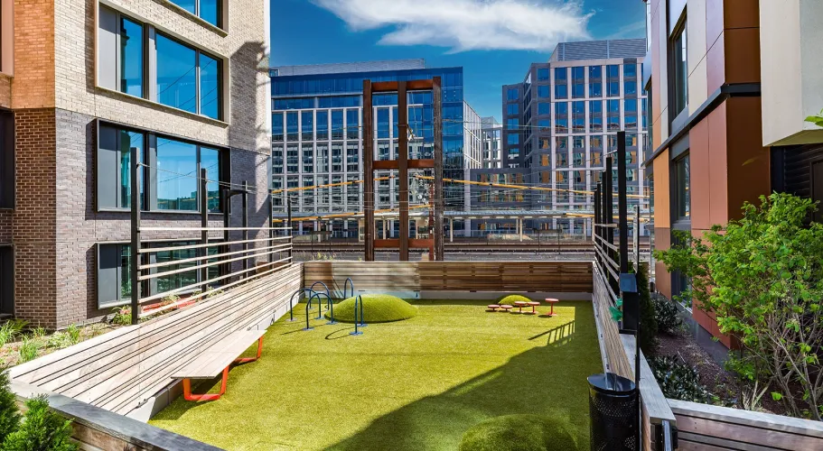 Urban outdoor play area with artificial turf, modern play structures, and scenic city views